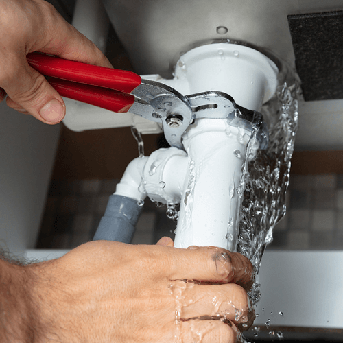 2 Sisters Plumbing technician fixing a leaking pipe under a sink in Johannesburg.